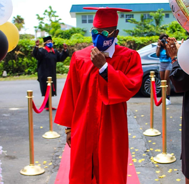 male student in cap and gown and mask